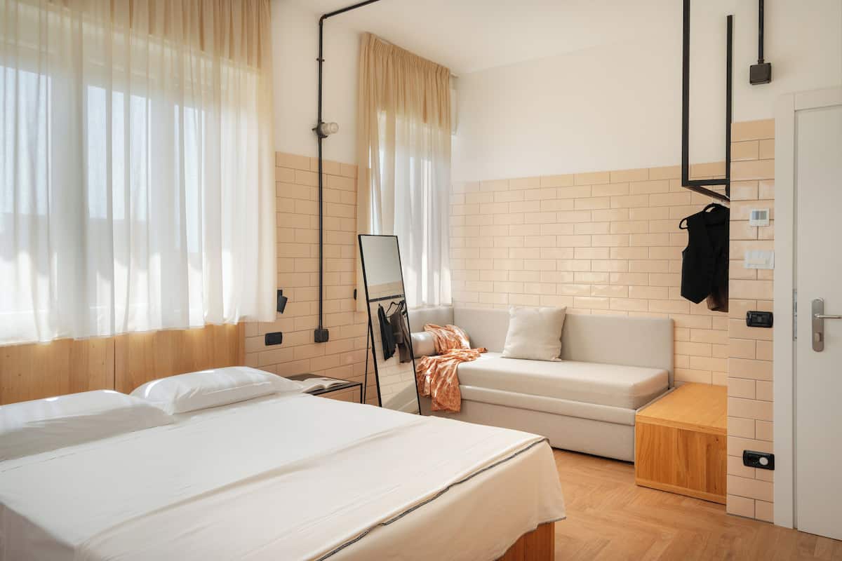 Une chambre d’hôtel comprenant un lit, un canapé, une table d’appoint en bois, un miroir et un porte-manteau mural.
