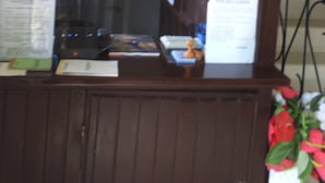 A room with a wooden paneled wall, a window with papers pinned to it, and a small table with a keyboard and a decorative item. - Hôtel Lobé (Kribi)