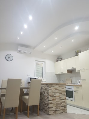 A modern kitchen with white cabinets, a stone accent wall, and recessed ceiling lights. - Apartman Ivan (Podstrana)