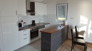 Una cocina moderna con armarios blancos, encimera de madera, horno empotrado y una ventana con persianas.