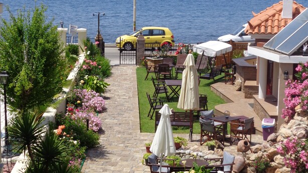 Un espace patio avec des sièges d’extérieur, une voiture jaune garée à proximité, et une vue sur la mer avec un voilier à l’horizon.