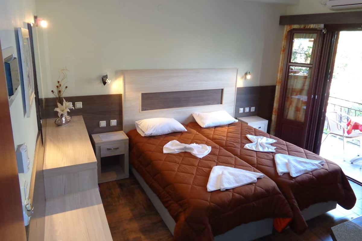 A hotel room with a large bed, two bedside tables, a nightstand, a mirror, and a window with curtains.