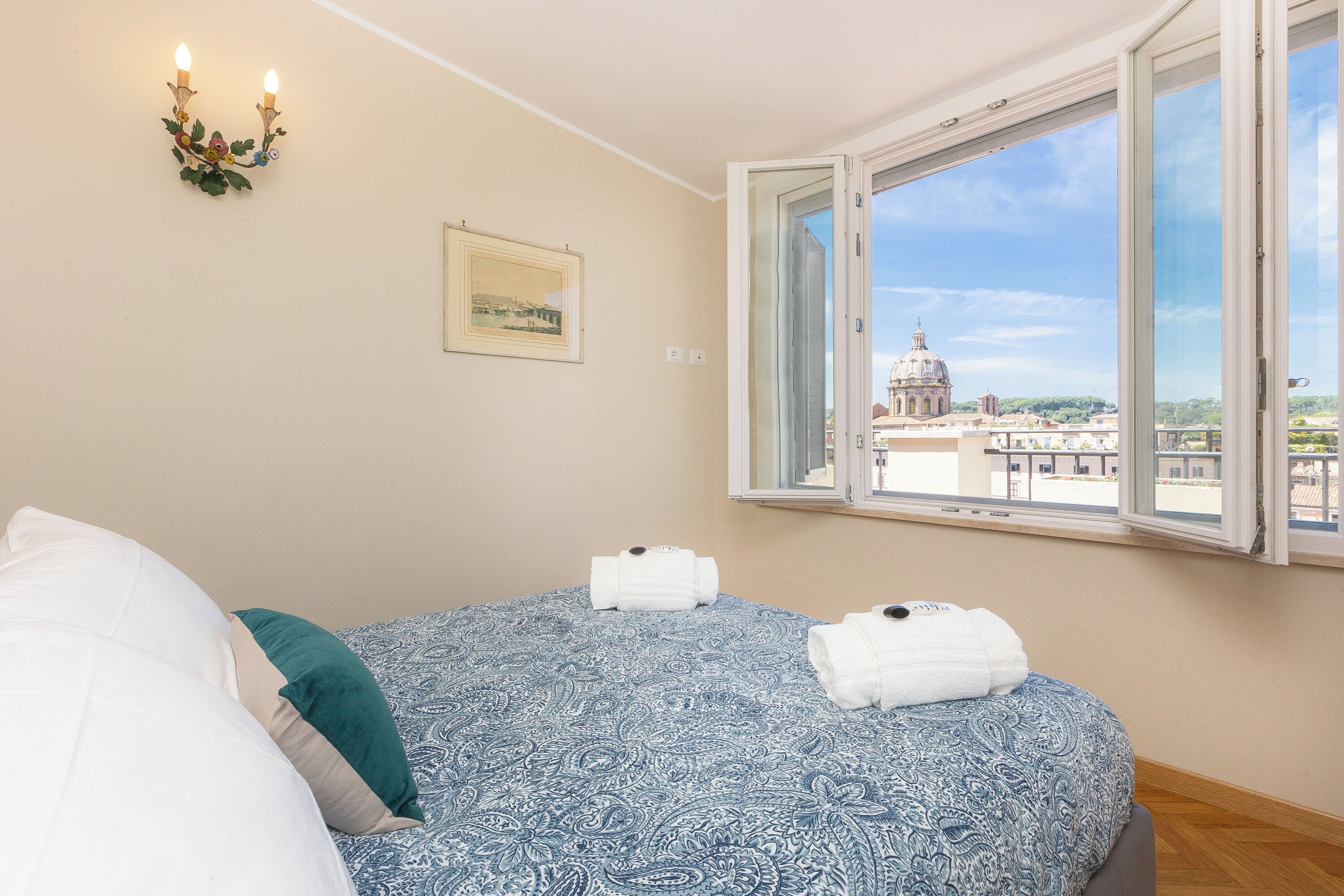 Une chambre à coucher avec un lit, une fenêtre donnant sur un immeuble et un luminaire fixé au mur.