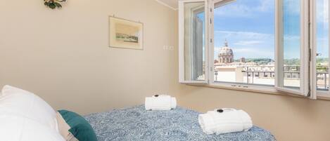 Un dormitorio con cama, ventana con vista a un edificio y una lámpara fijada a la pared.