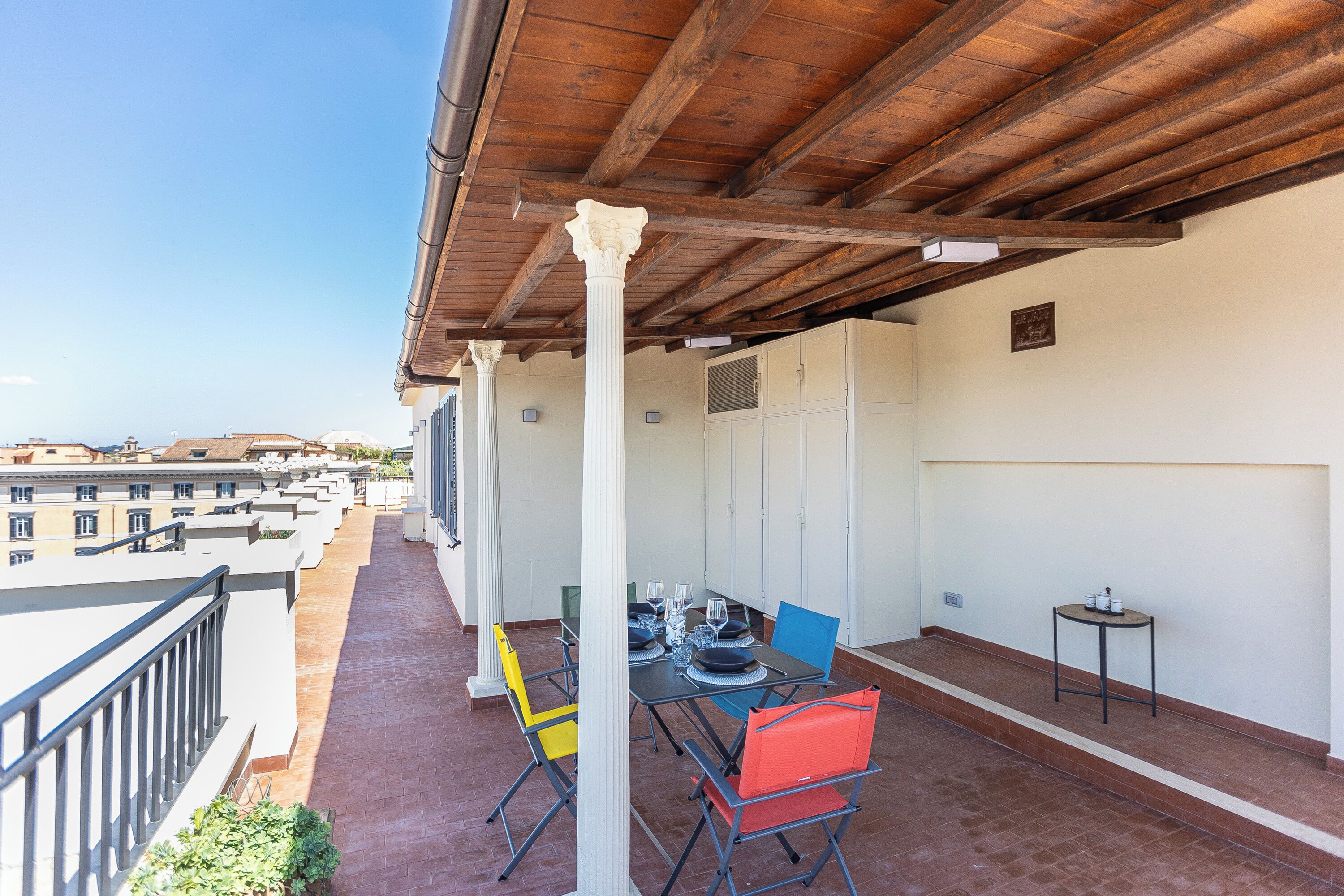 A balcony with a table set for dining, chairs, and a small table with items on it.