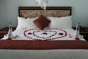 A bed with rose petals arranged in a heart shape, a red pillow, and two water bottles on either side. - Solyana Hotel (Bahir Dar)