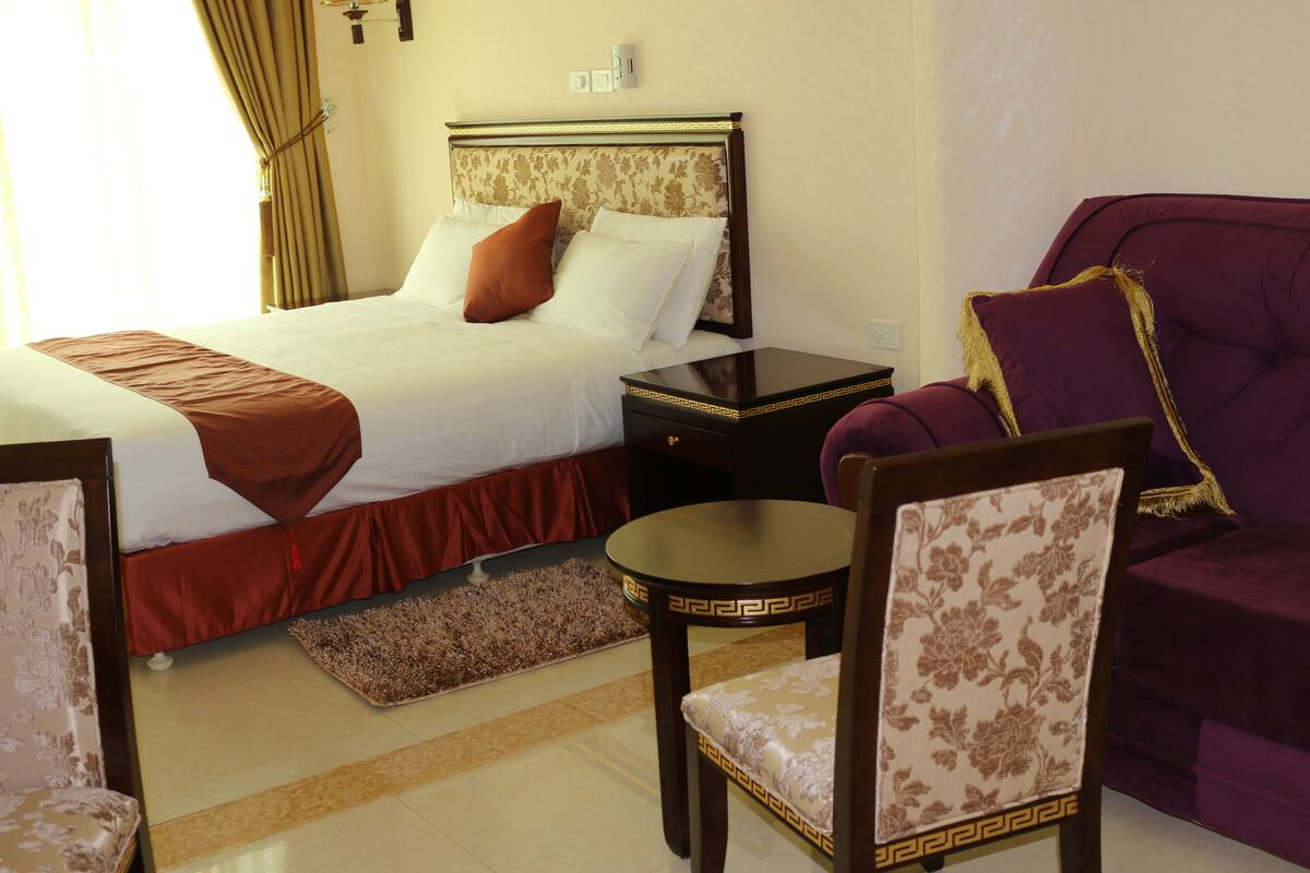 A hotel room with a bed, a nightstand, a chair, a table, and a sofa.