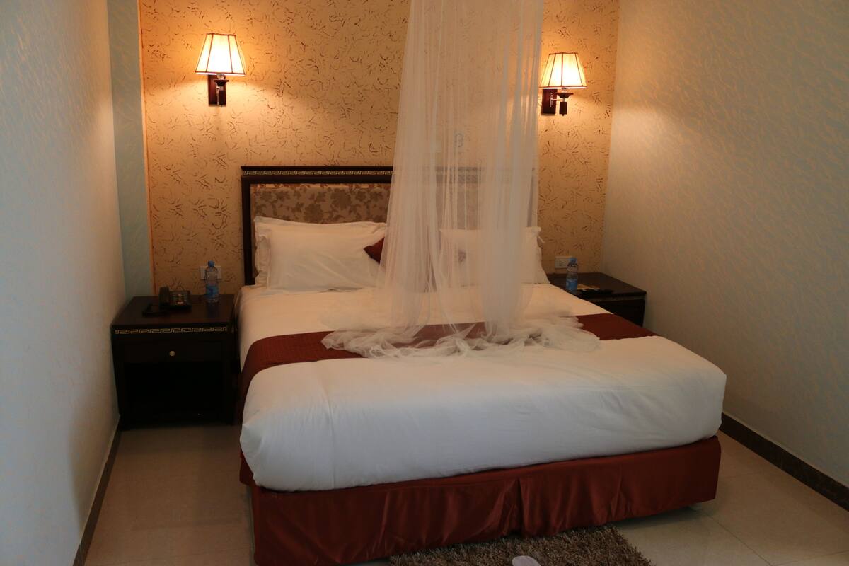 A hotel room with a large bed, two bedside lamps, a nightstand, and a water bottle on the nightstand.