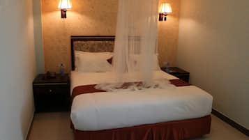 Une chambre d’hôtel avec un grand lit, deux lampes de chevet, une table de chevet et une bouteille d’eau sur la table de chevet.