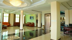 A spacious lobby with a chandelier, leather sofas, a reception desk, and a polished floor.