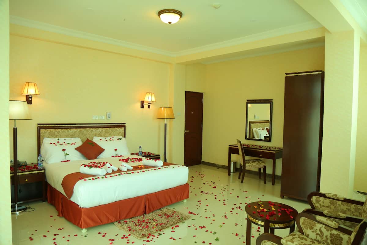 A hotel room with a large bed, two bedside tables, a desk, a chair, and a wardrobe.