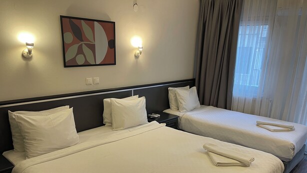 Hotelkamer met twee bedden, een nachtkastje, een wandlamp en een raam met gordijnen.