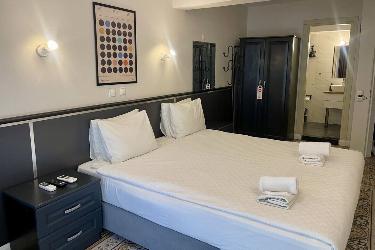 A hotel room with a bed, bedside tables, a wardrobe, a mirror, and a wall-mounted light fixture.