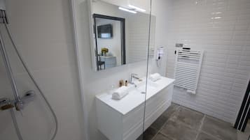 Un baño moderno con ducha envuelta en vidrio, dos lavamanos y un espejo grande.