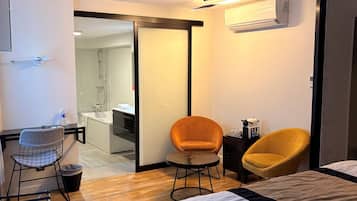 Una habitación de hotel moderna con cama, dos sillas, escritorio y baño visible a través de una puerta abierta.
