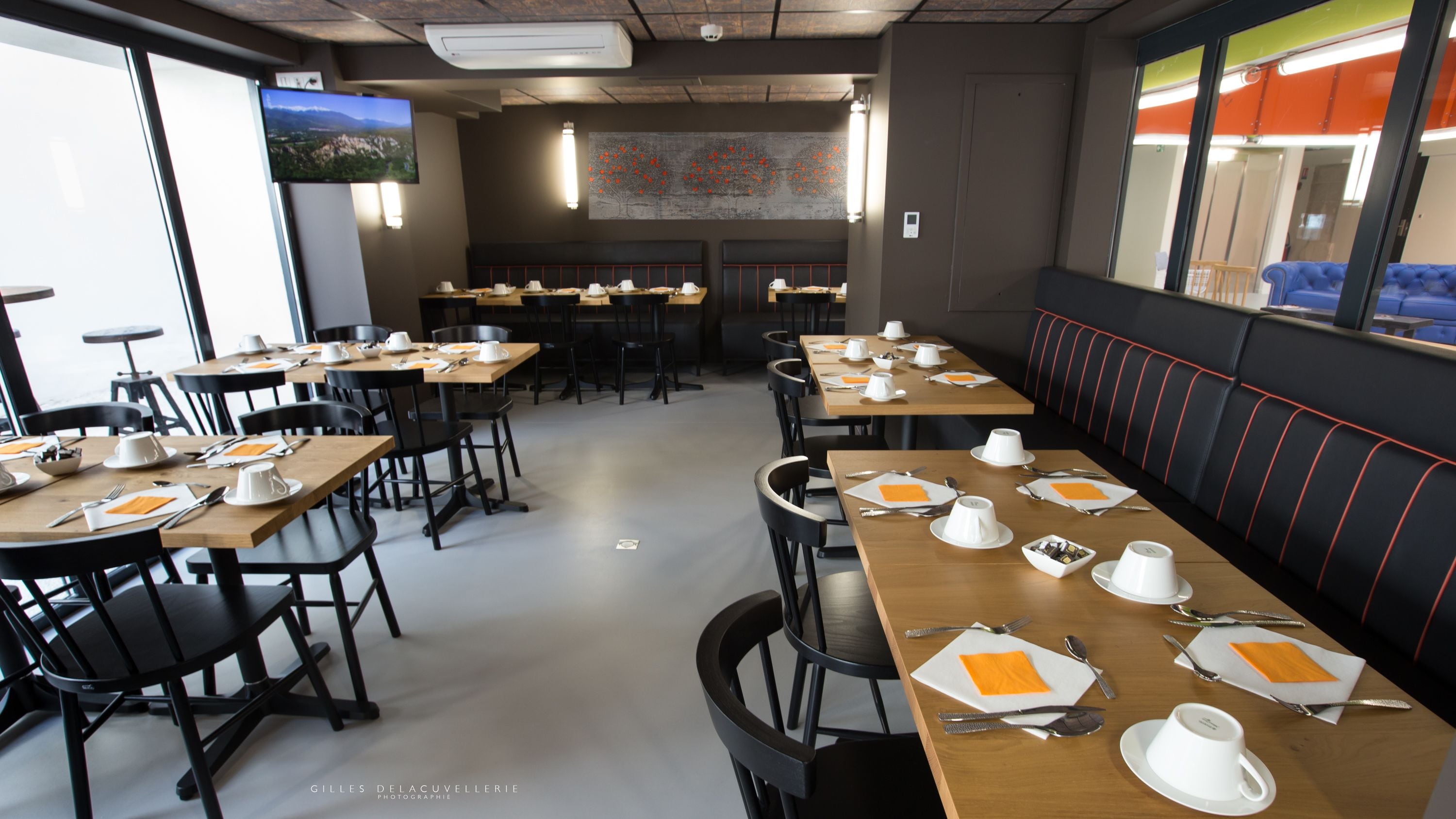 A restaurant with multiple tables set for dining, chairs, and a large screen displaying a landscape.