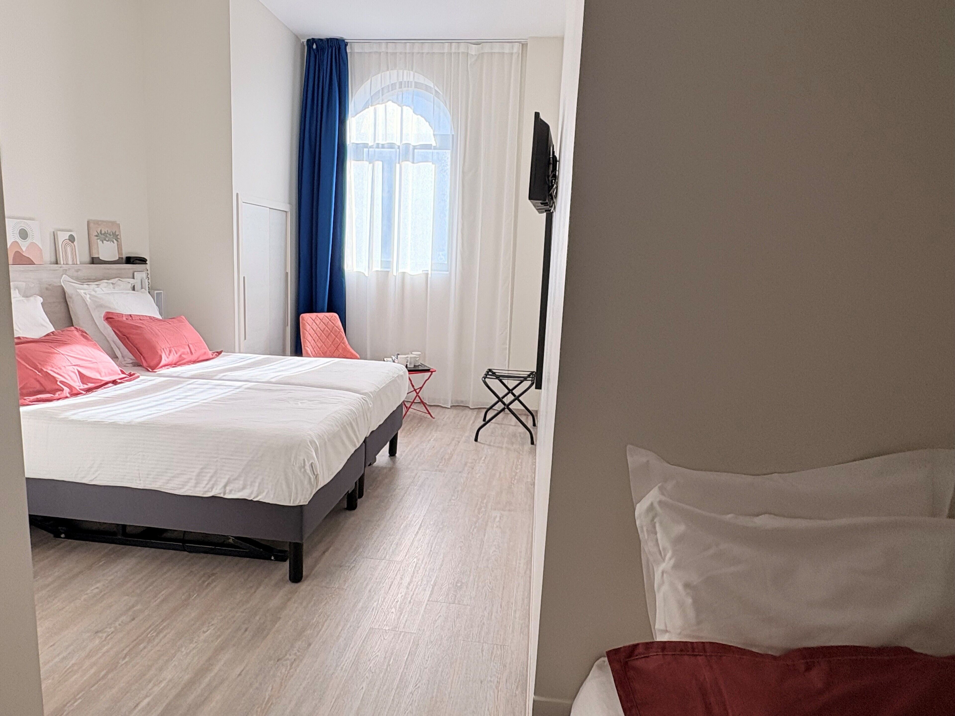 A modern hotel room with a large bed, a small table, a chair, and a TV mounted on the wall.