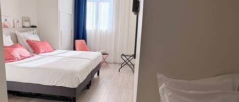A modern hotel room with a large bed, a small table, a chair, and a TV mounted on the wall.