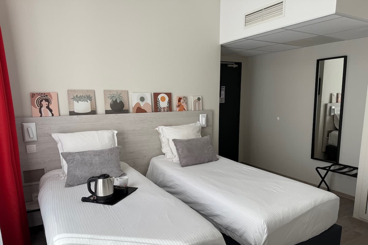 Une chambre d’hôtel avec deux lits, une machine à café et un miroir.