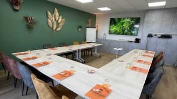 Un salón de conferencias con una larga mesa, sillas, una pizarra y elementos decorativos en la pared.