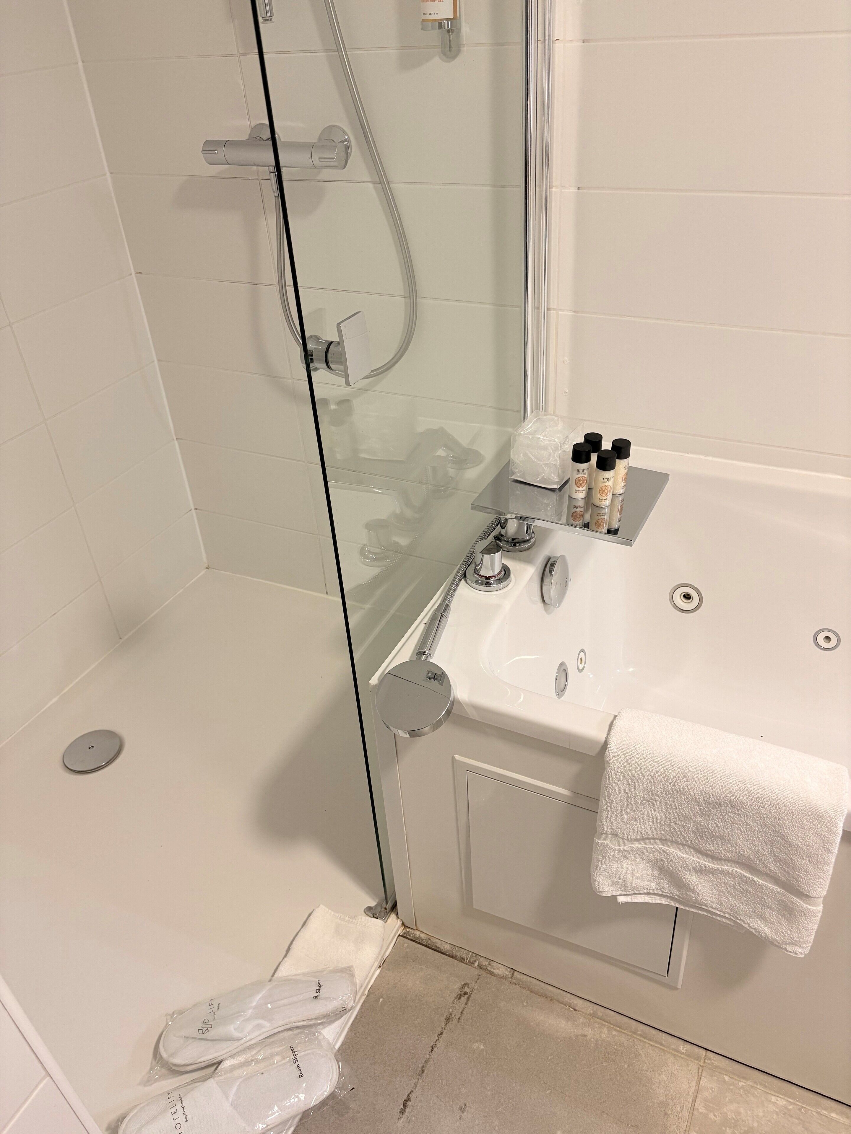 Un baño con ducha de mampara de vidrio, lavabo con artículos de aseo y una toalla colgada en la pared.