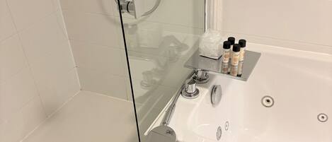 Un baño con ducha de mampara de vidrio, lavabo con artículos de aseo y una toalla colgada en la pared.