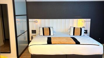 Una habitación de hotel moderna con una cama grande, suelo de madera, una silla amarilla y un diseño de techo original.