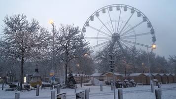 Un parc enneigé avec une grande roue, des arbres sans feuilles et quelques personnes qui se promènent.