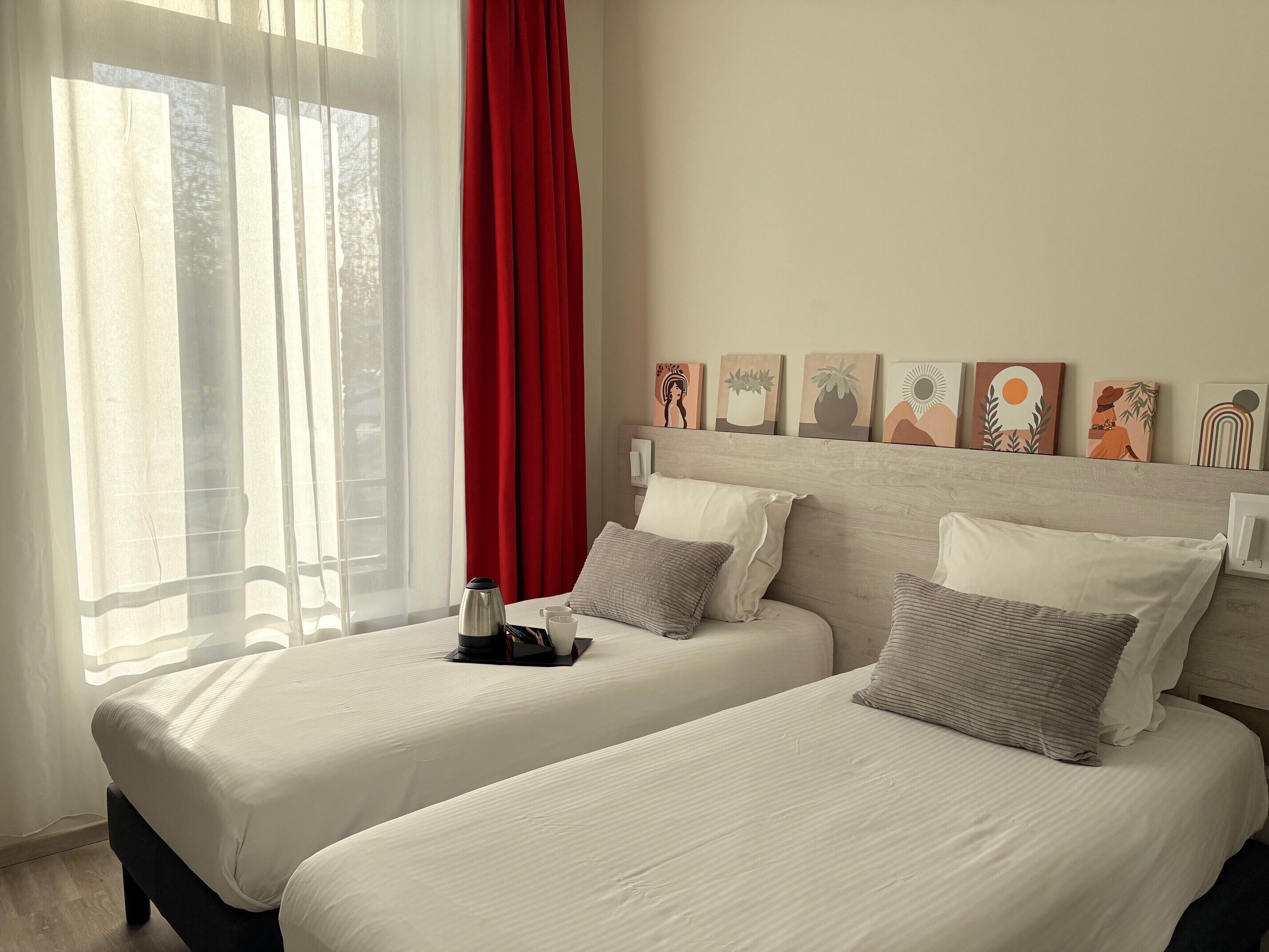A hotel room with two beds, a coffee table, and a window with sheer curtains and a red curtain.