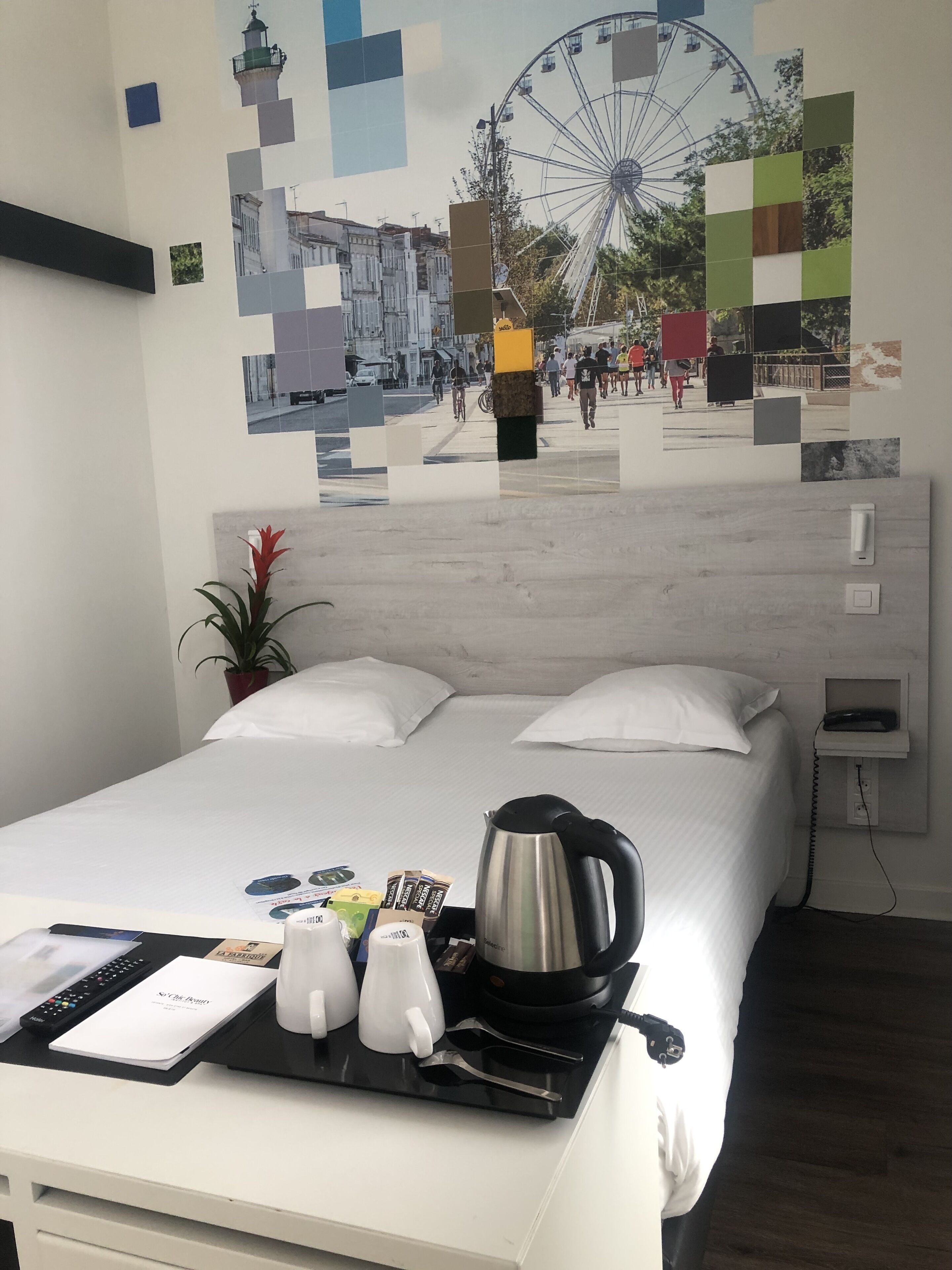 A hotel room with a bed, a coffee maker, a tray with cups and a menu, and a wall with a Ferris wheel mosaic.