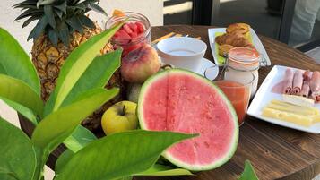 Une table avec une variété de fruits, un croissant, un sandwich au jambon et un verre de jus.