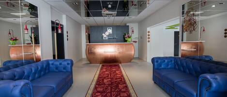 A modern reception area with a central desk, two blue sofas, a patterned carpet, and a decorative ceiling.
