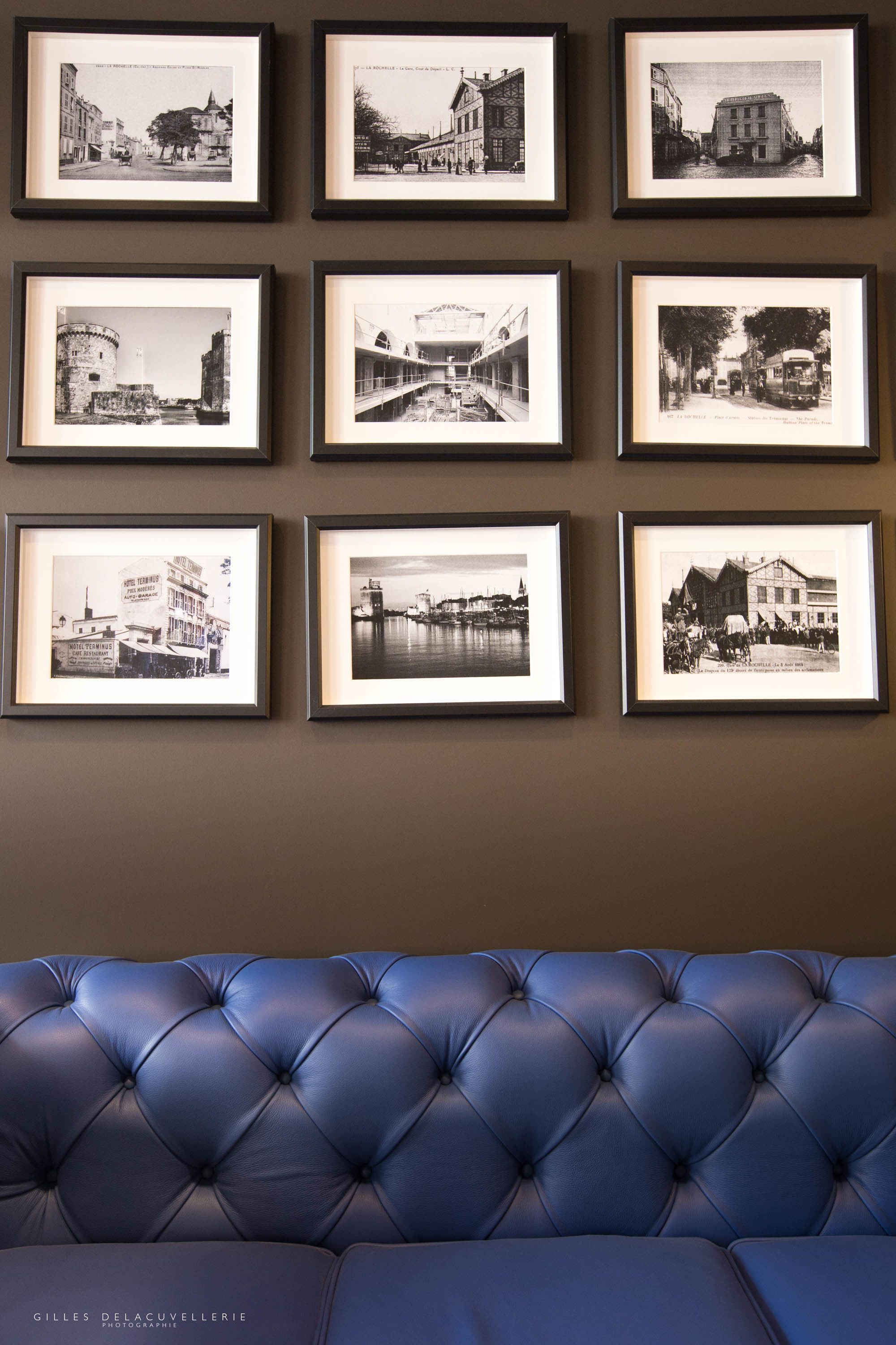 Una pared con nueve fotografías en blanco y negro, enmarcadas, de diferentes edificios y paisajes.