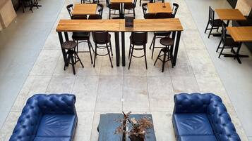 Un espace intérieur spacieux avec de nombreuses tables et chaises, un canapé bleu central et une plante décorative.