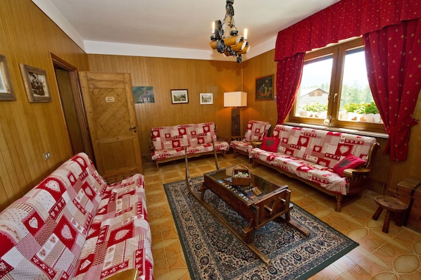 A cozy living room with wooden walls, two sofas with patterned covers, a coffee table, and a chandelier.