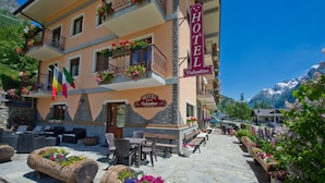 A hotel with outdoor seating, flower planters, and a mountain view. - Hotel Valentino (Bionaz)