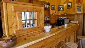 A wooden bar area with a rustic design, including a wooden counter, stools, and a window with a view. - Hotel Valentino (Bionaz)