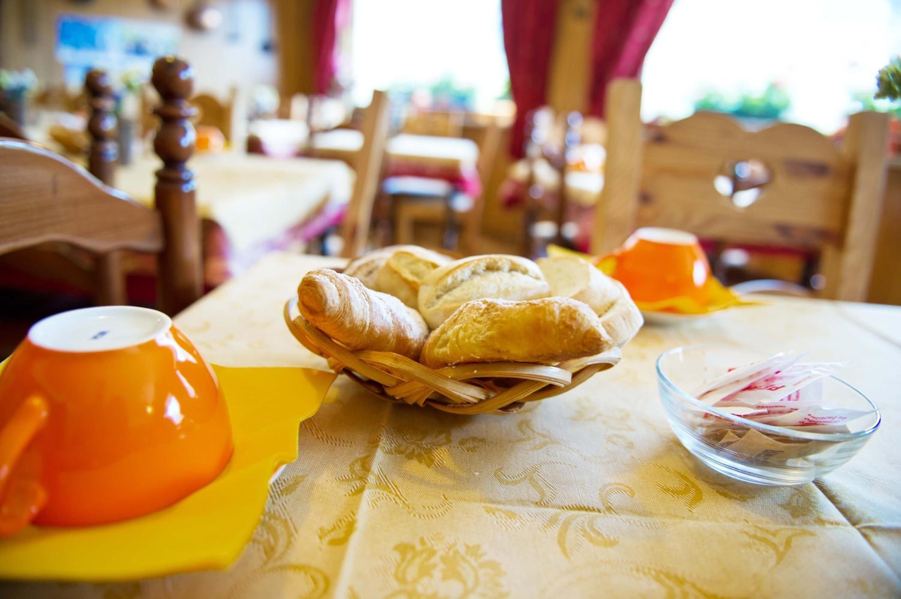 Ein Esstisch mit einem Brotkorb, einer Schüssel mit Beilagen und zwei orangenen Tassen.