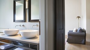 Un baño con dos lavamanos grandes de color blanco, un espejo y un perchero para toallas.