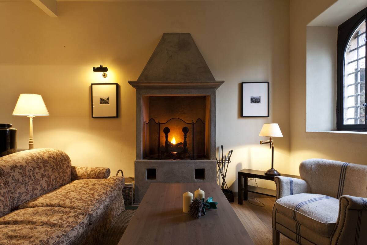 A cozy living room with a fireplace, patterned sofas, a wooden coffee table, and framed pictures on the walls.