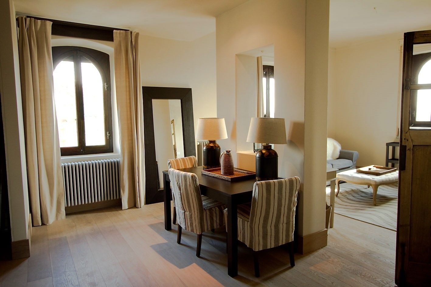 A hotel room with a dining area, a sofa, and a window with curtains.
