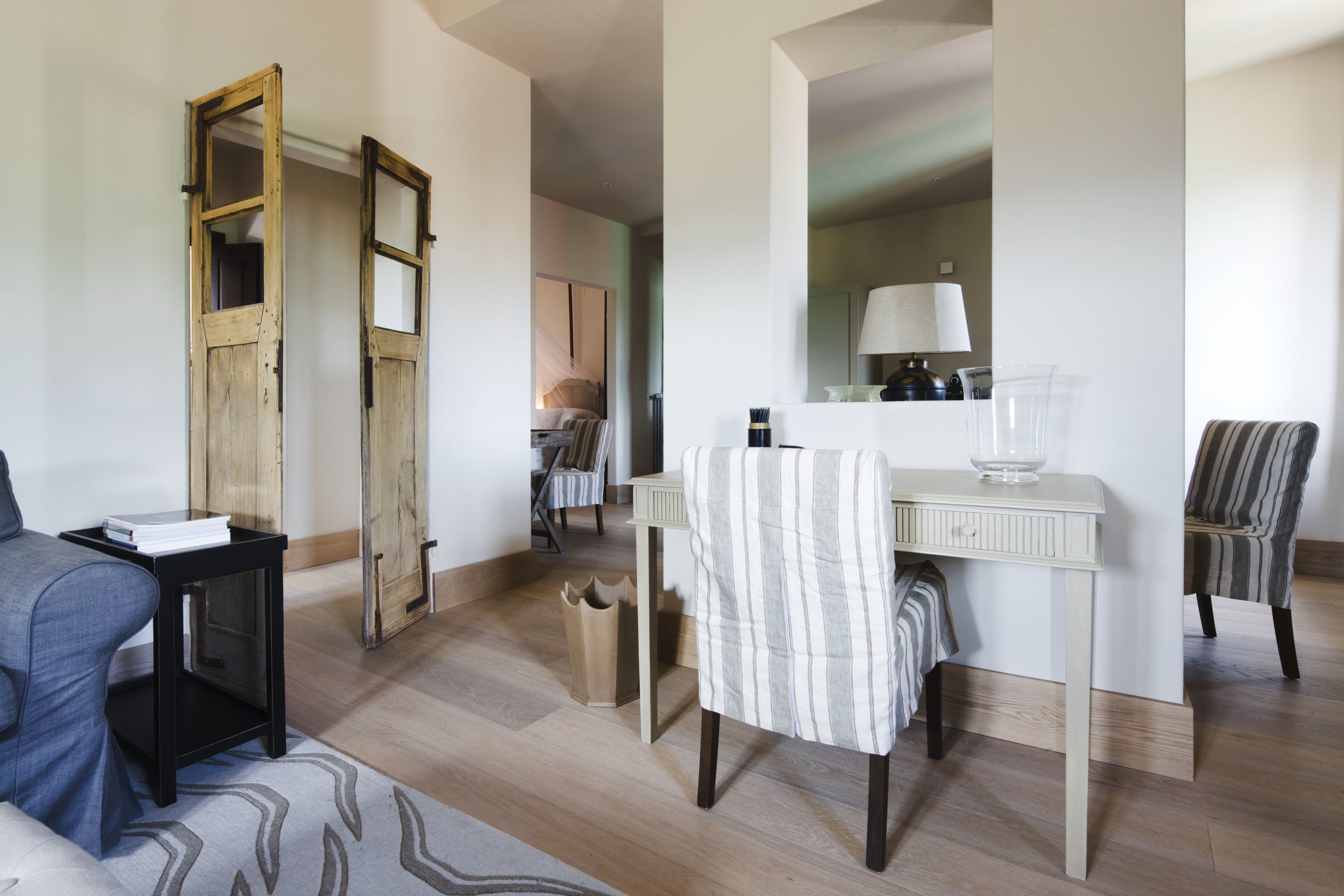 A modern living room with a sofa, a striped armchair, a small table with a lamp, and a wooden door with glass panels.