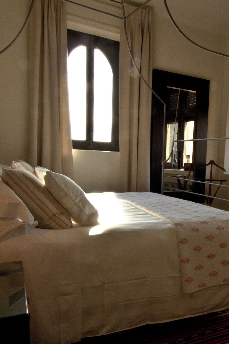 A bed with a white bedspread and pillows, a window with curtains, and a door with a mirror.