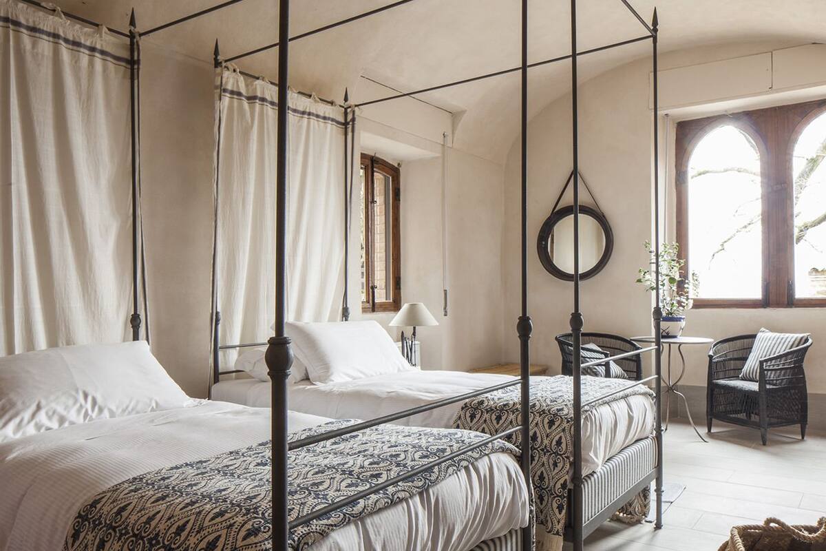 A four-poster bed with a canopy, two bedside tables, a chair, and a window with a view of trees.