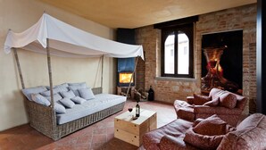 Una sala de estar acogedora con un sofá de mimbre, un sofá rojo estampado, una mesa de centro de madera y una cama con dosel blanca.
