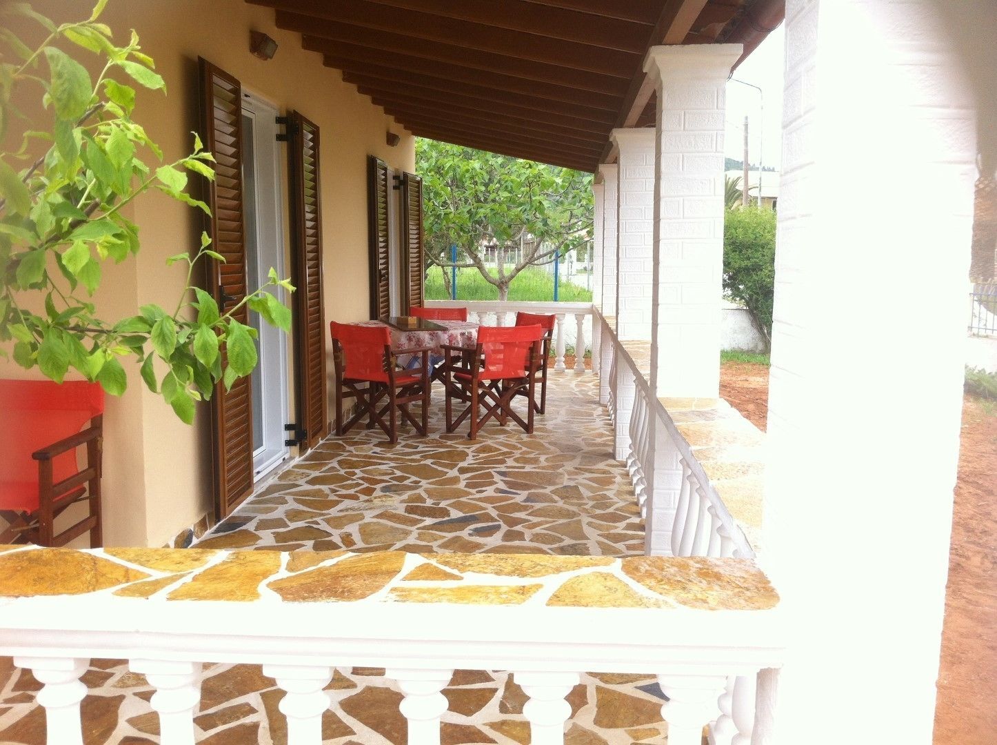 A covered patio with a stone floor, a table with chairs, and a view of greenery outside.