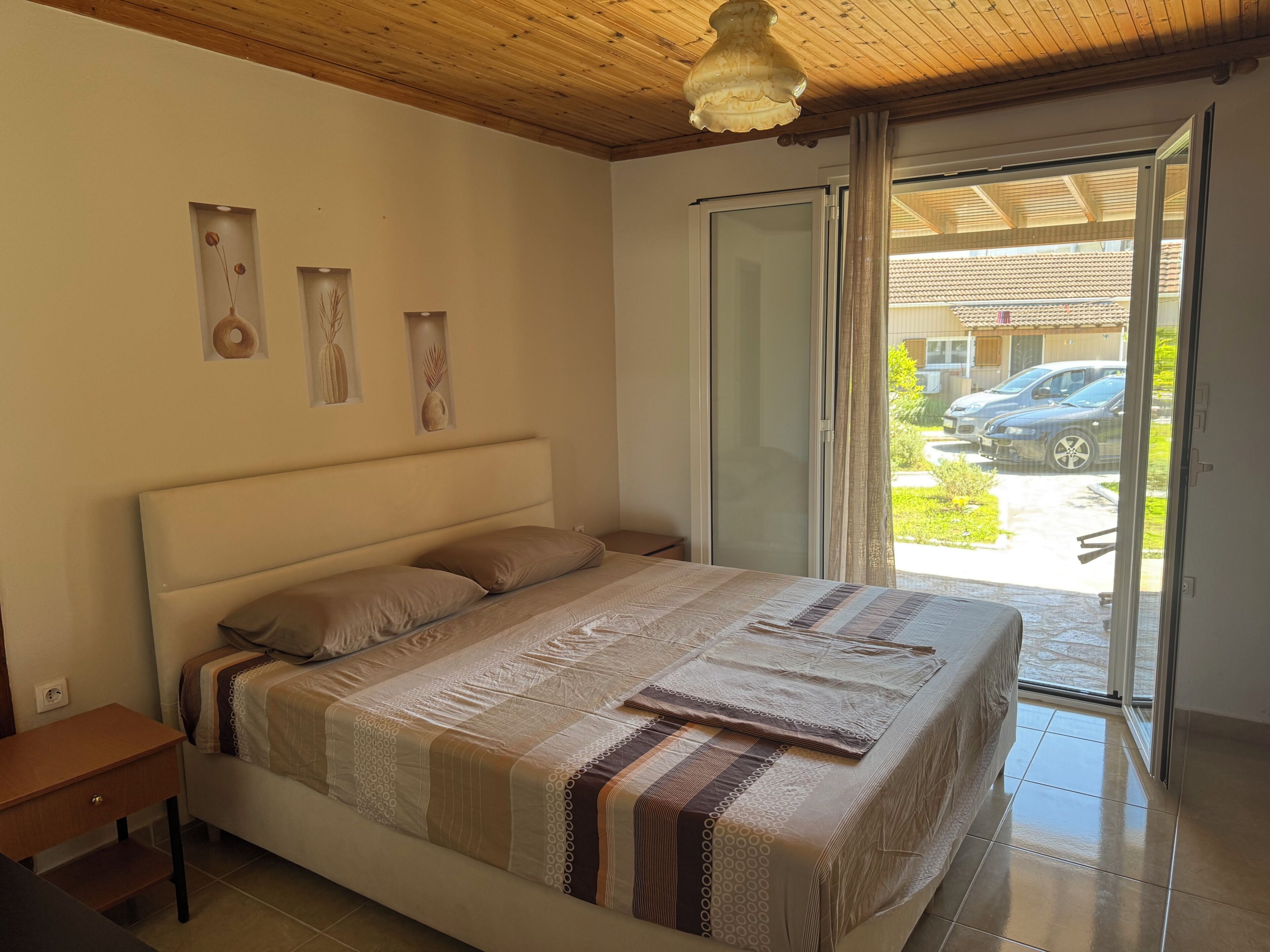 Una camera da letto con un letto, un comodino, soffitto in legno, una porta scorrevole in vetro e vista sull'esterno.