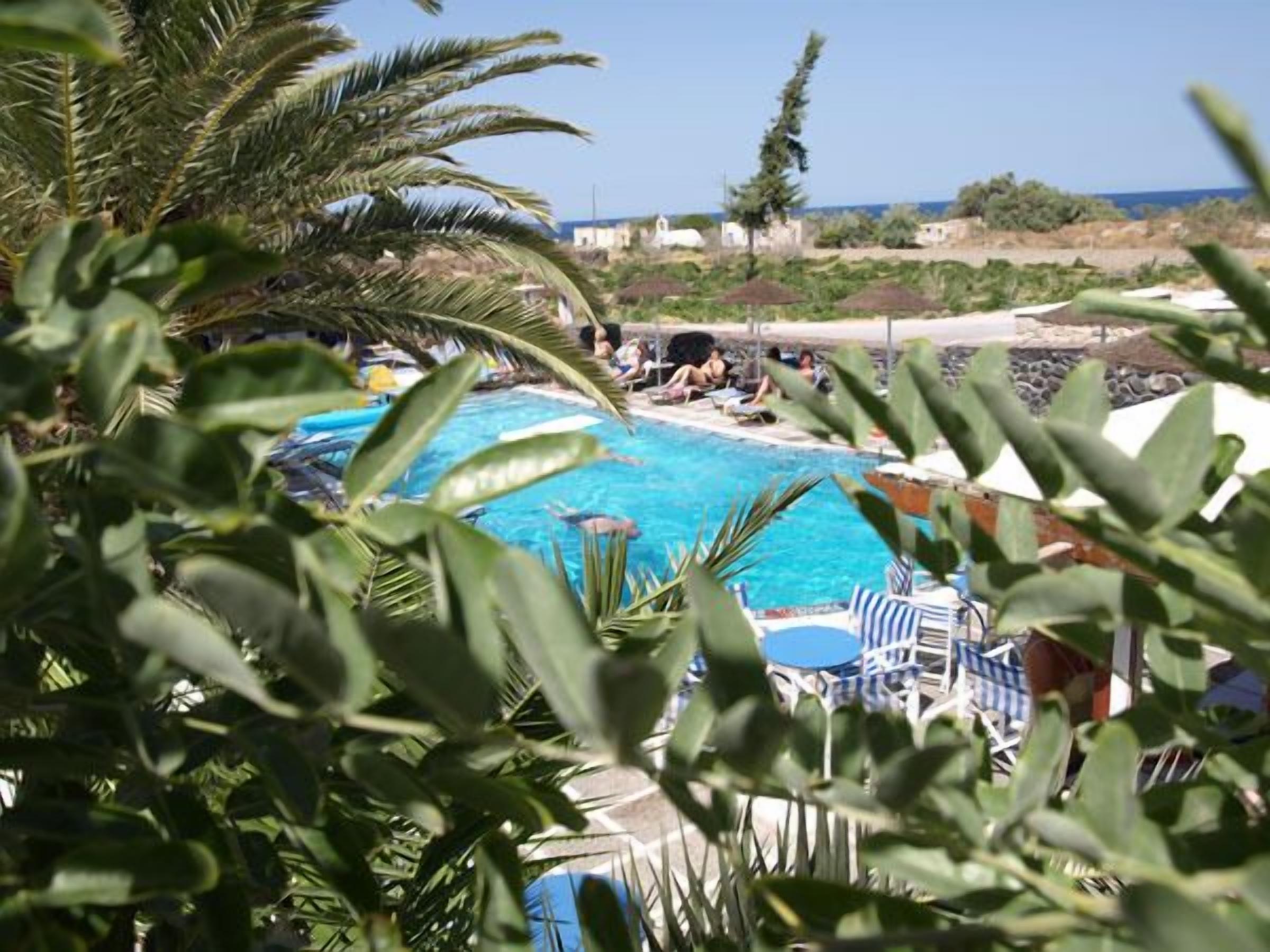 Un espace piscine doté de chaises longues et de parasols, entouré de verdure et offrant une vue sur un plan d’eau.