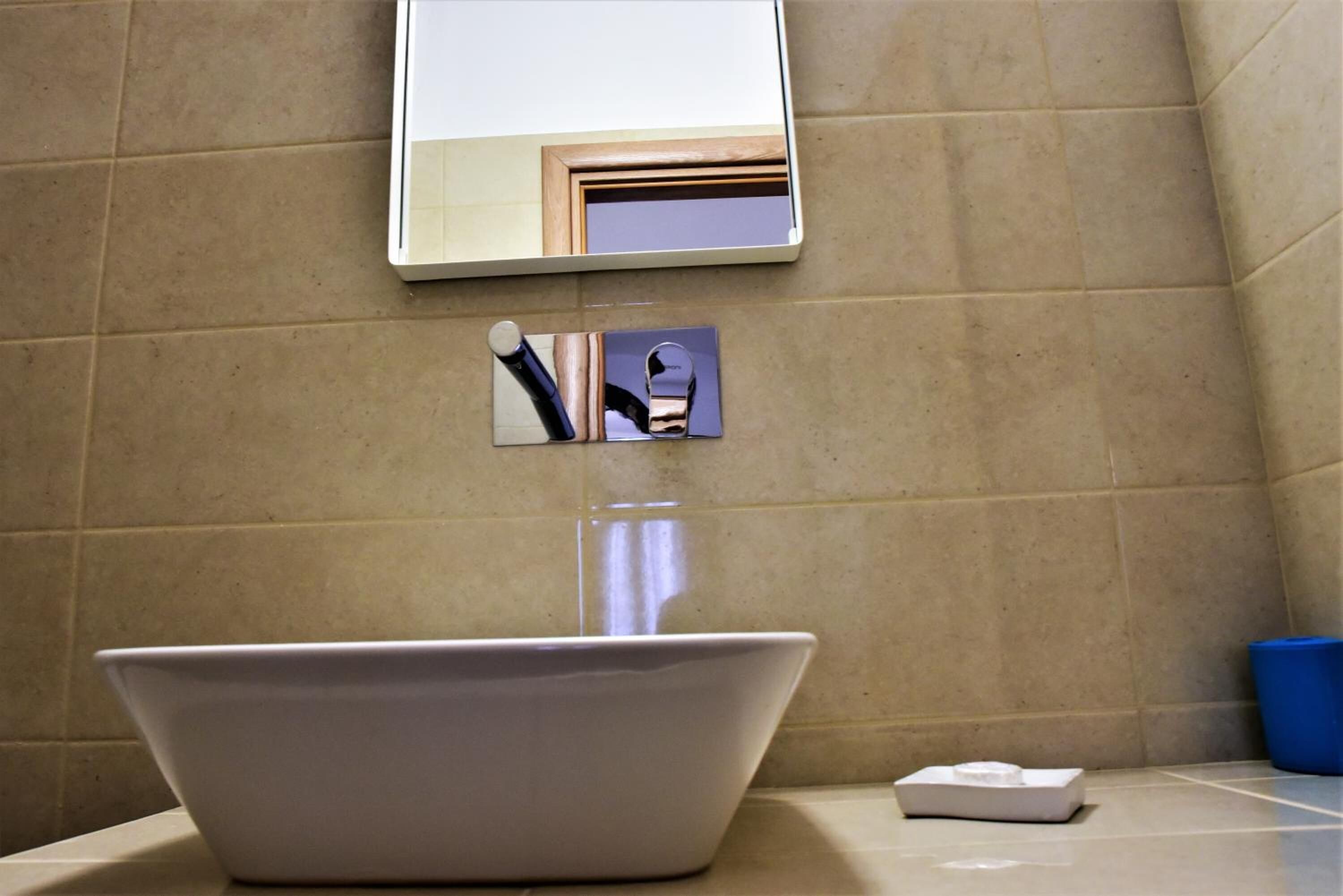 Un baño con un lavamanos blanco, un espejo y un bote de basura azul.