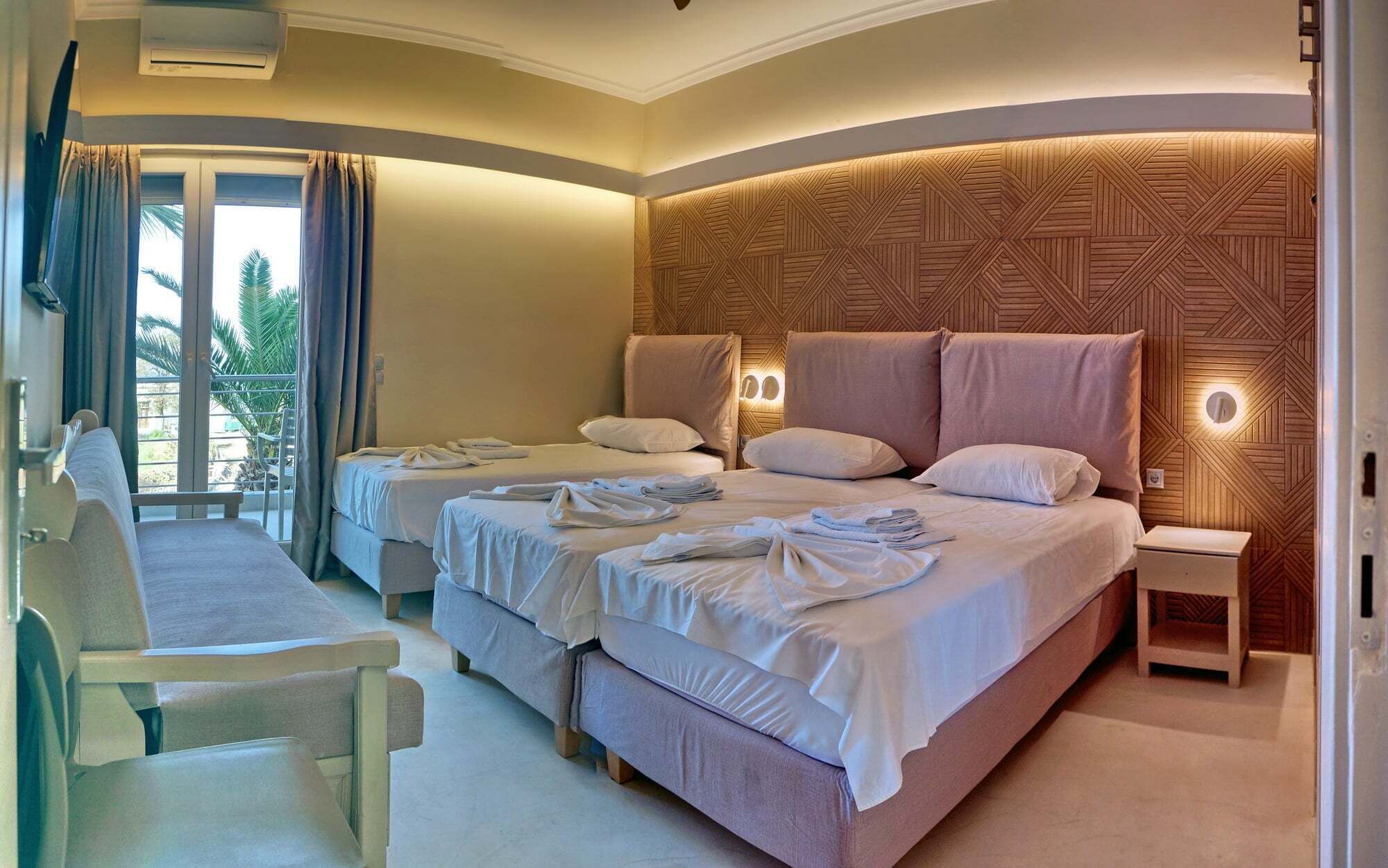 A hotel room with a large bed, two bedside tables, a chair, and a balcony with curtains.
